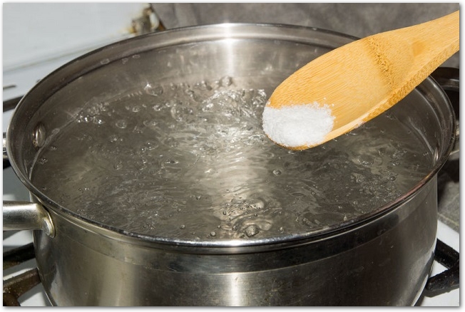 沸騰した鍋に木のスプーンで塩を入れている様子